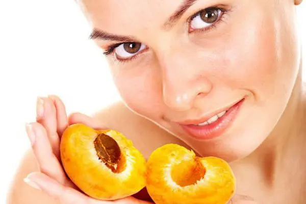 Лицо девушки и половинки абрикоса в руках