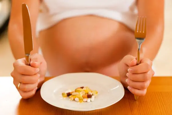 Беременная сидит перед тарелкой с таблетками